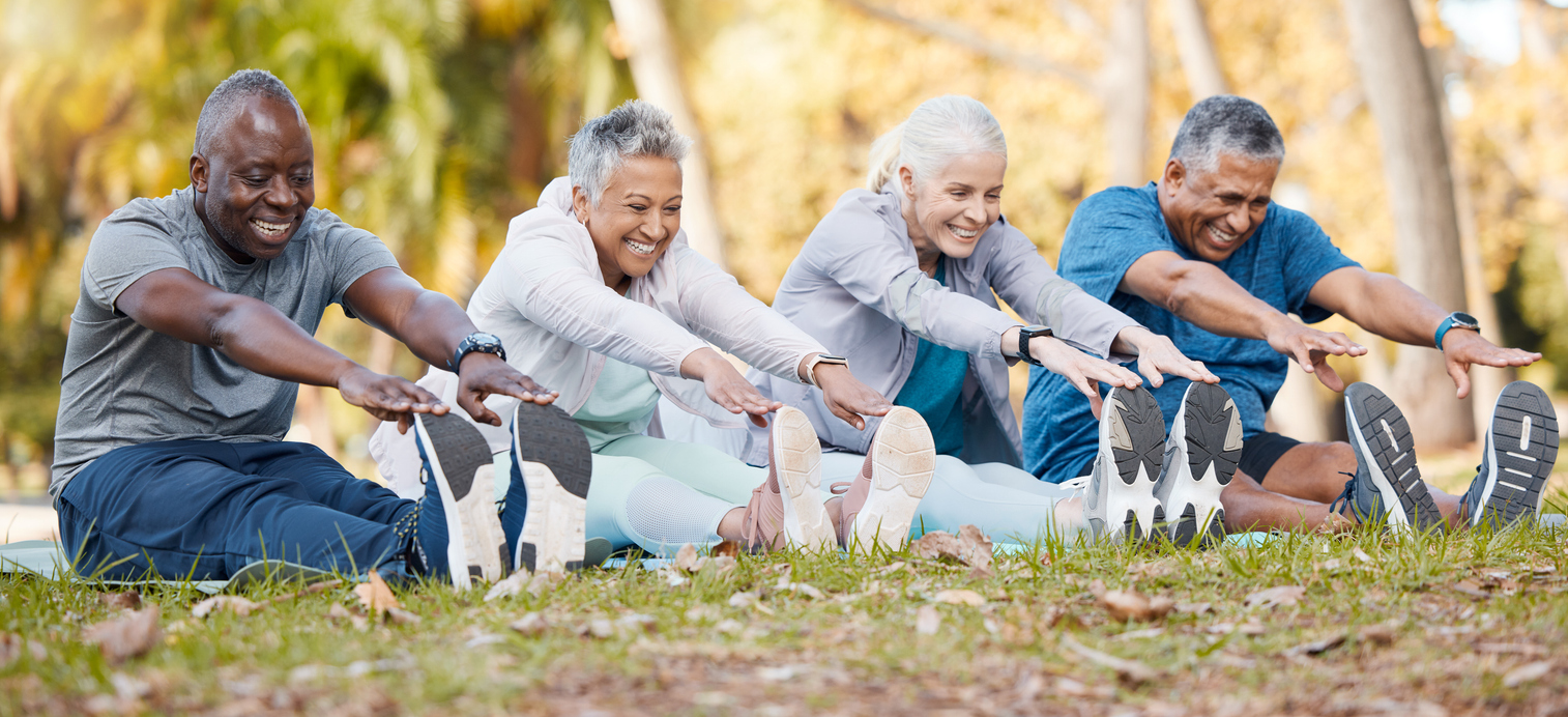 Four older adults in workout clothes sitting on the ground touching their toes 